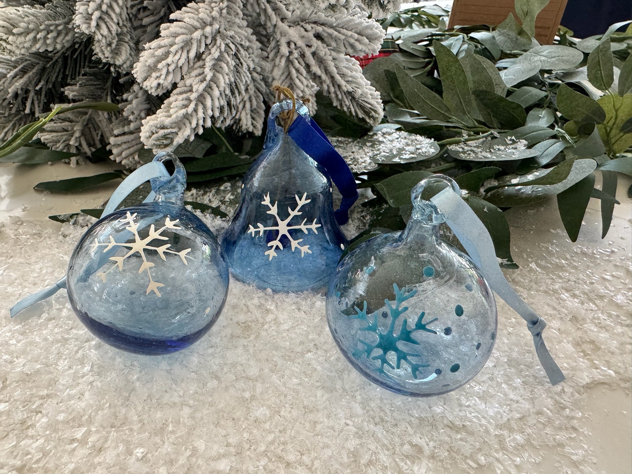 Blue glass ornaments from Bethlehem with snowflake designs with snow and greenery in the background.